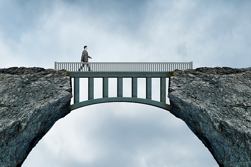 A businessman walks across a bridge that spans two large rocky cliffs