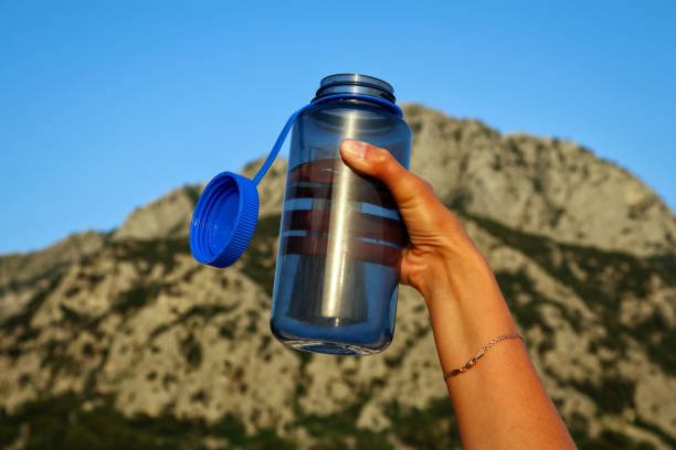 Tourist reusable bottle in hand on the background of the mountain Tourist reusable blue bottle in a woman's hand on a mountain background blue reusable water bottle stock pictures, royalty-free photos & images