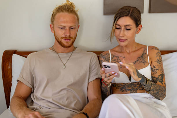 istock Modern Caucasian couple, lying in bed, while using laptop and mobile phone 1406945364