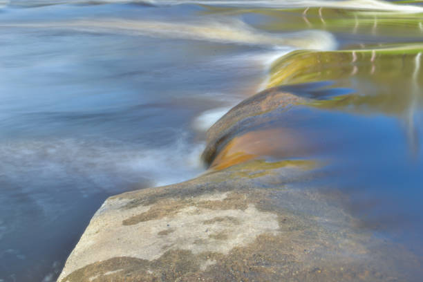 istock gray boulder in the river rapids washed by blue water which is blurred in a long exposure. 1406948497