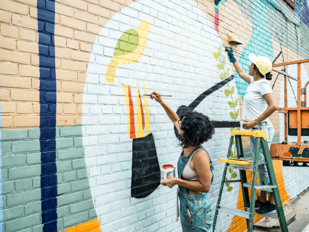 dos artistas femeninas pintando grandes murales murales - street entertainment fotografías e imágenes de stock