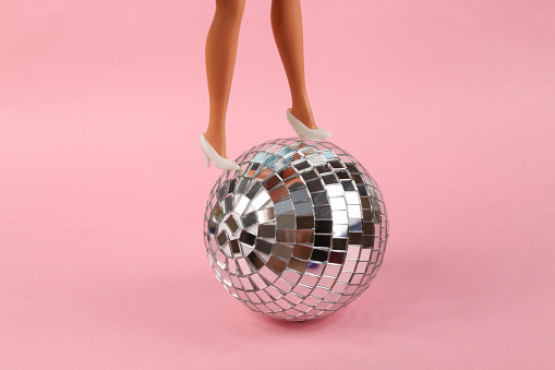 Minimal party concept. Doll feet with a disco ball on pink background. Creative layout