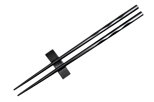Close-up of black chopsticks placed on a resting base isolated on white background.