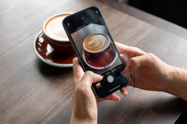 Hands woman using Iphone 13pro taking photo of a cup of latte in cafe for post in social media stock photo