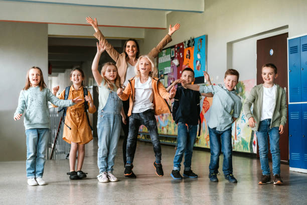 Cheerful students jumping with teacher in school corridor stock photo