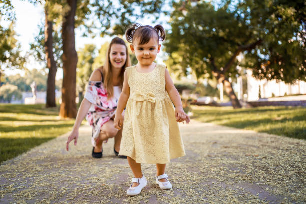 istock Mother looking at daughter making her first steps in the park on a warm summer day 1406954970