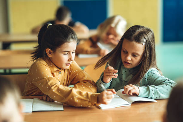 Girl explaining female friend while doing homework in classroom