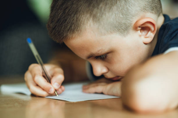 Male student writing on book at desk in classroom