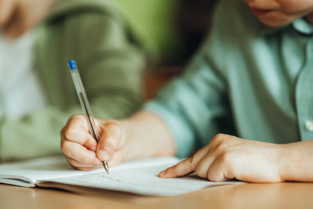 istock Midsection of boy writing in book while studying by friend at school 1406955142