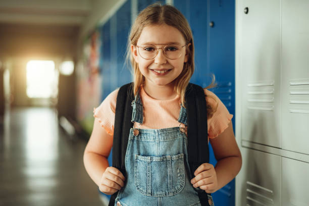 Portrait of schoolgirl with eyeglasses standing by locker in corridor stock photo