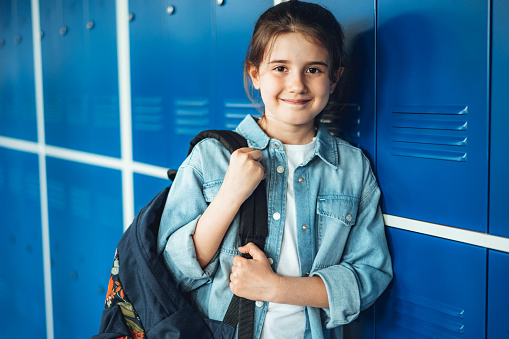 Portrait of smiling girl with backpack standing by blue locker in corridor