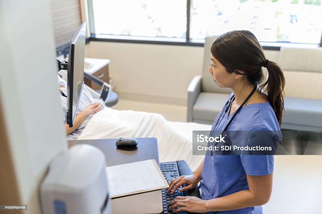 Female doctor works quietly on computer while patient rests The mid adult female doctor works quietly on the computer while the unrecognizable patient sleeps. Nurse Stock Photo