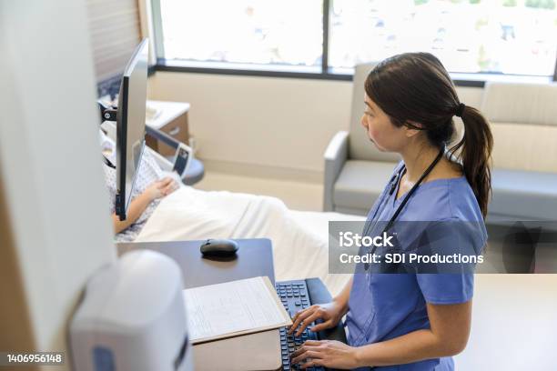Female Doctor Works Quietly On Computer While Patient Rests Stock Photo - Download Image Now
