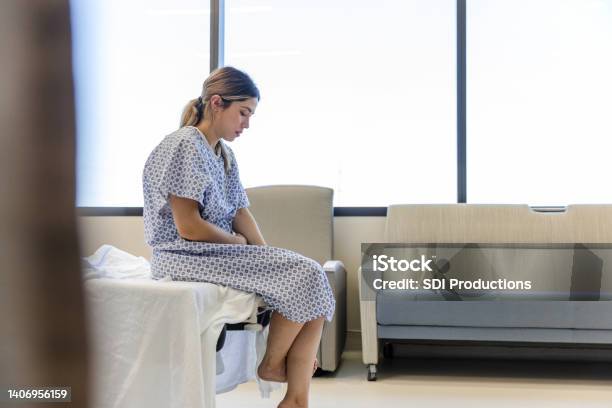 Anxious Sad Young Woman Wearing Hospital Gown Looks Down Stock Photo - Download Image Now