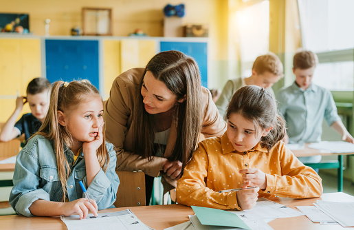 Teacher talking with schoolgirls at desk in classroom