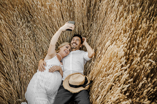 Young couple taking a selfie while lying down in wheat field