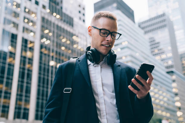 istock Cheerful formal adult male using headphone while browsing mobile on street 1406957897