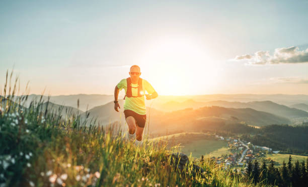 active mountain trail runner dressed bright t-shirt with backpack in sport sunglasses running endurance marathon race by picturesque hills at sunset time. sporty active people concept image. - running jogging mountain footpath imagens e fotografias de stock