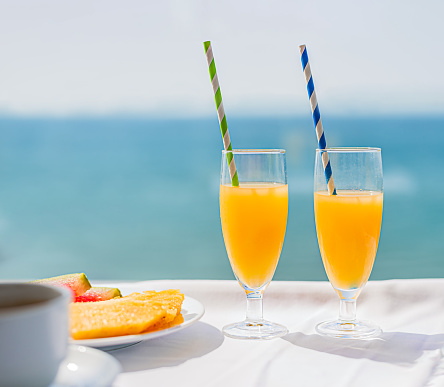 detail of two glasses of orange juice on a white table and a blue background of the mediterranean sea. vacation and health concept. colorful.