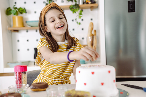 Cute girl decorating cake in the kitchen. She is happy and cheerful