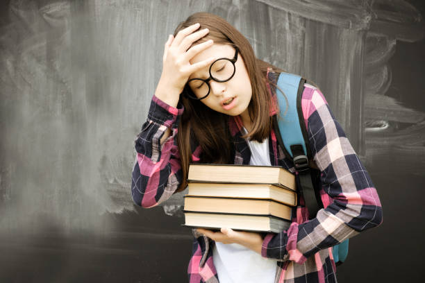 ragazza adolescente con il dito puntato alla lavagna. ragazza studentessa adolescente in camicia, occhiali con zaino blu e appunti su sfondo nero lavagna. educazione, scuola e concetto di persone. spazio di copia - student effort book carrying foto e immagini stock