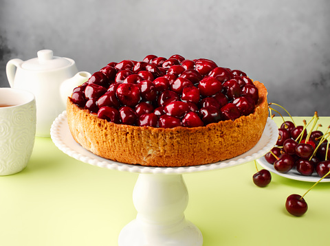 Open vegan cherry pie on the kitchen table, on a cake pan, on a colored green background. Fruit cake. Tart. Cherry pastries with fresh berries. Summer berry vegan pie. Top view, copy space, close up.