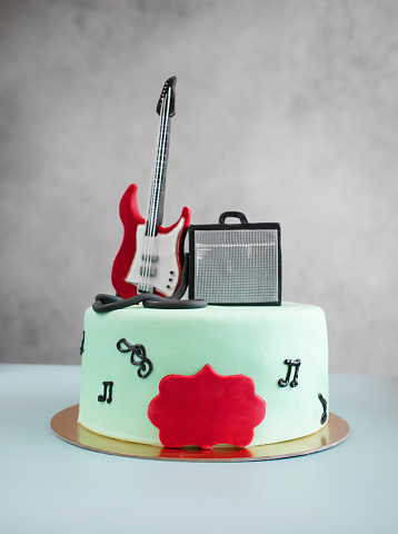 Musical themed cake with a guitar on top as a decoration. Sweet food for the musician's birthday. A gift to a creative person, a singer. Surprise for the guitarist. Top view, copy space, close up.