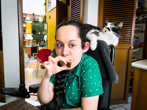 Disabled girl eating chocolate at home with her cat