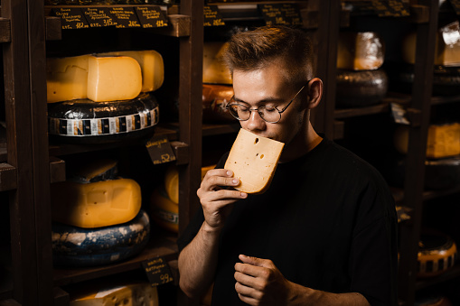 Handsome buyer in cheese shop sniff and enjoy limited gouda cheese. Snack tasty piece of cheese for appetizer