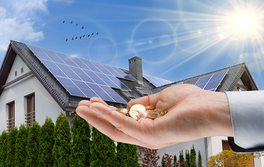 Solar panel on roof of house and coins in hand. Concept of money saving and clean energy.