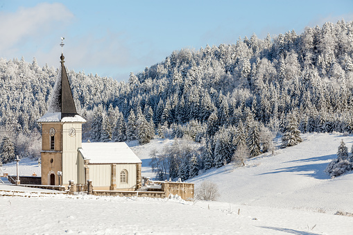 Landscape in Les Piards, Jura, France. In the city of Nanchez, there is a church in front of a Wonderfull natural landscape composed of pine tree, blue sky, and fresh snow.