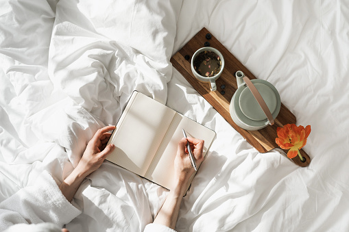 High above view of person making notes using notebook and pen, kettle and morning coffee, romantic mood, cozy bedroom interior design, home decor, flat lay