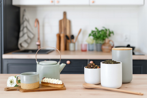 Herbal tea in mugs and jars as well as eclair on wooden table. Kettle usage. Tea drinking concept. Home comfort. Morning time. Cozy flat idea