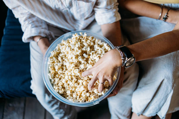 An Unrecognizable Mixed-race Couple Enjoying Eating Popcorn While Relaxing At Home A from above view of an anonymous Asian woman and her Indian boyfriend eating snacks while spending their leisure time together. Popcorn stock pictures, royalty-free photos & images