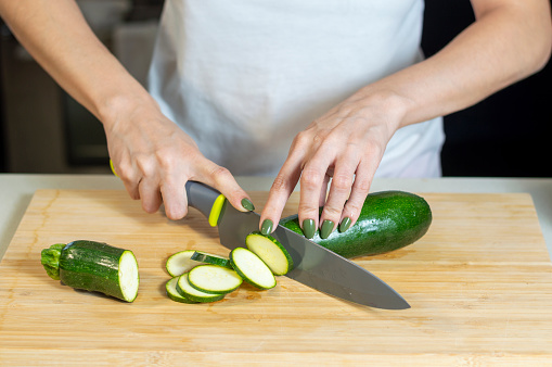 Close up of young woman hands cutting zucchini on wooden cutting in Madrid, Community of Madrid, Spain