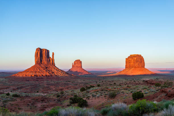 berühmte aussicht monument valley buttes und horizont bei leuchtend rotem sonnenuntergang buntes licht in arizona mit orangefarbenen felsformationen und plänen mit blauem himmel - merrick butte stock-fotos und bilder