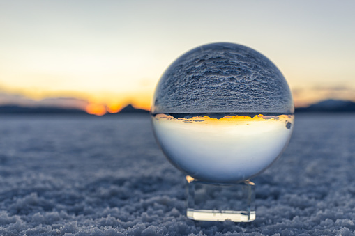 Crystal ball macro closeup of view in round glass globe on stand with reflection of Bonneville salt flats and mountains at colorful sunset in Utah desert landscape