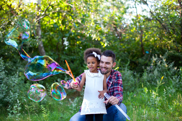 Happy father and daughter playing soap bubbles in park.