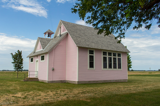 This image shows a close-up view of an old pink painted historic country school house exterior with windows, built in the 1800’s in the midwestern USA.