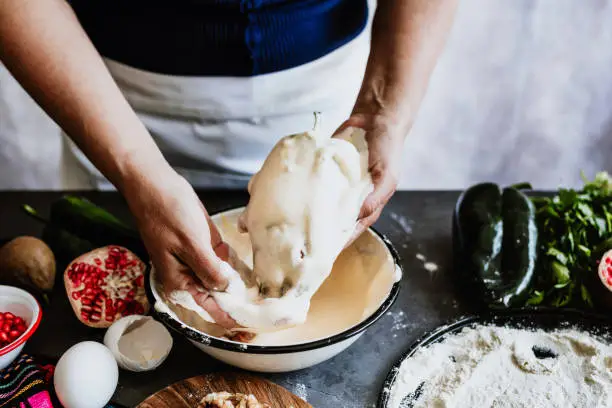 cooking mexican battered chiles en nogada recipe by woman hands with Poblano chili and ingredients, traditional dish in Mexico