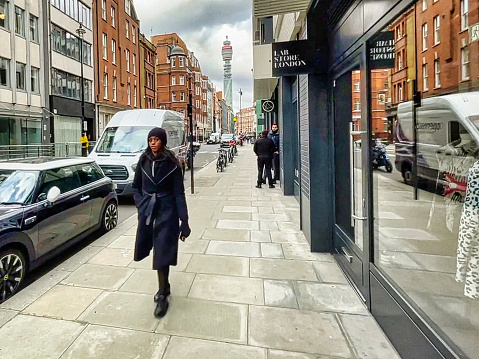 London, United Kingdom - March 07 2022: an afro american woman is walking on the sidewalk of a small street of the british capital
