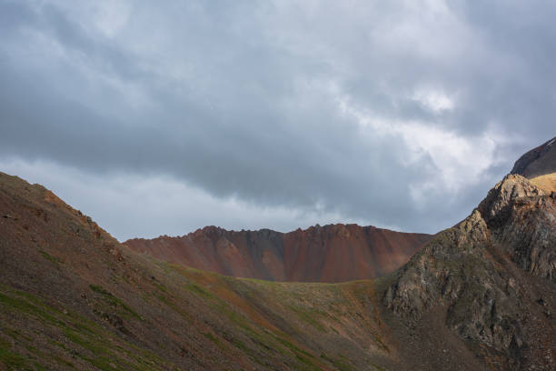 istock Dramatic alpine landscape with wide sharp mountain ridge under gray cloudy sky. Dark atmospheric mountain scenery with large sharp rocks on ridge top under rainy clouds in gray sky at overcast weather 1407007152