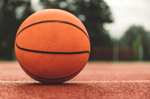 Focus on a basketball on the ground on an outdoors basketball court.
