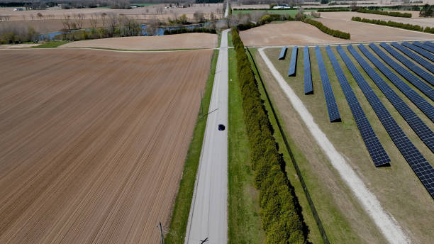 An aerial photo behind a car driving between a solar farm and rural field. stock photo