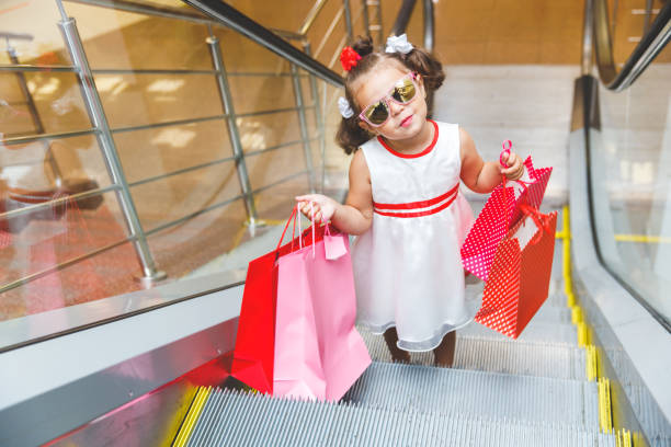 色とりどりのバッグを持つモールのエスカレーターでサングラスをかけた小さな女の子 - escalator child shopping mall little girls ストックフォトと画像
