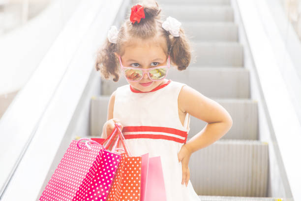 モールのエスカレーターに乗った小さな女の子が色付きのバッグを持っている - escalator child shopping mall little girls ストックフォトと画像