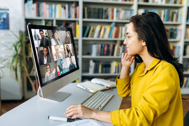 istock Online education. A female student learning online at home, focused watching at a computer monitor on which a group of other students and a teacher telling information 1407014775