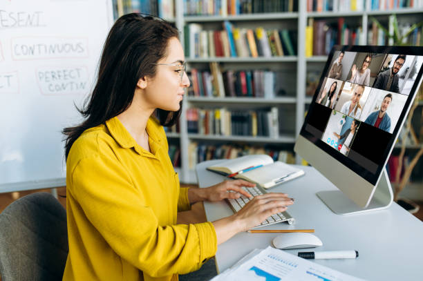 istock Online education. A female student learning online at home, focused watching at a computer monitor on which a group of other students and a teacher telling information 1407014778