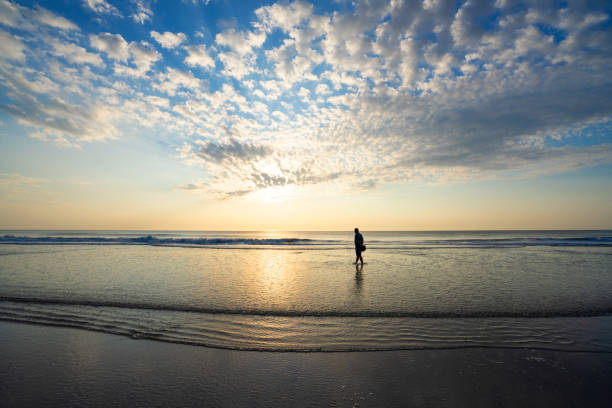Senior man walking on beach at sunrise. Beautiful cloudy sky reflected on the beach. Jacksonville, Florida, USA.