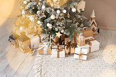 Wrapped gifts under the Christmas tree in a bright interior with garland lights in bokeh.